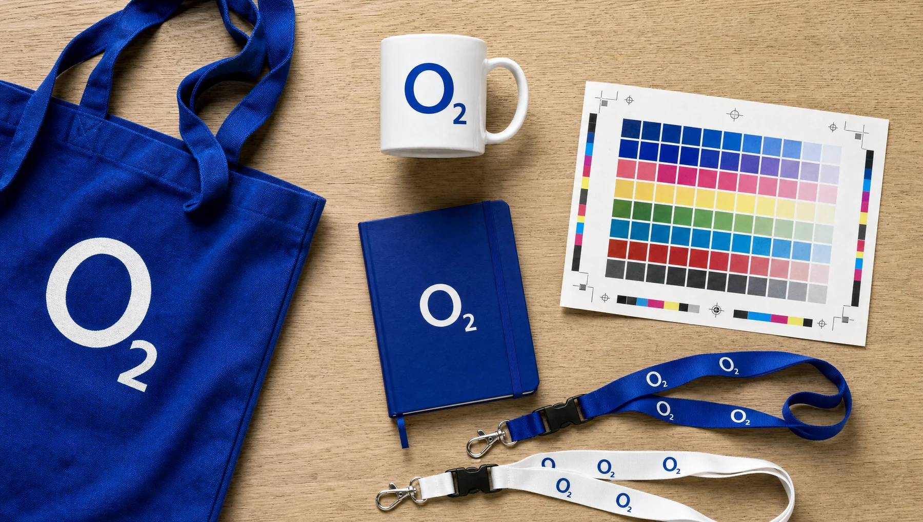 O₂-Tasche, Notizbuch, Tasse und Schlüsselbänder neben einem Druckfreigabe-Muster.